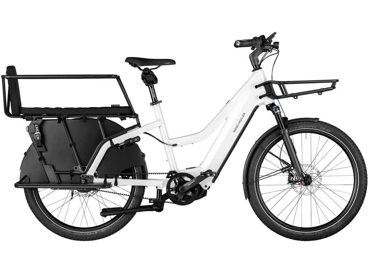 Ein weißes Riese & Müller Multicharger Mixte GT Fahrrad, mit schwarzen Vorderrad-Gepäckträger und schwarzen Gepäckträger hinten der mit einen schwarzen Gerüst an der Radnabe ünterstützend befestigt ist.